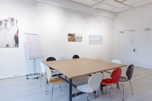 Atelier-dieSmartphotoschule Eine Person sitzt an einem Schreibtisch mit einem großen Computerbildschirm, auf dem verschiedene digitale Inhalte angezeigt werden. An der Wand vor ihr hängen zahlreiche Bilder und Texte, die sich mit kreativen Konzepten und Ideen beschäftigen, darunter auch Illustrationen und Fotografie. Der Raum ist hell und modern eingerichtet, mit Reflexionen von Pflanzen und Lichtern im Fenster. Der Kontext deutet darauf hin, dass es sich um eine Arbeitsumgebung handelt, in der KI-generierte Bilder und kreatives Storytelling eine Rolle spielen.