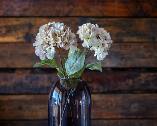 Detailreiche Nahaufnahme von Kunstblumen in Vase mit gezieltem Schärfespiel: Vordergrund scharf, Hintergrund weich verschwommen.
