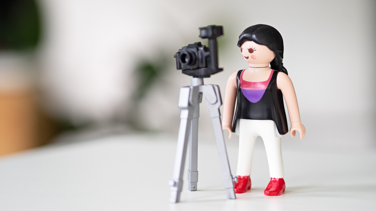 Eine kleine Spielfigur steht neben einer Kamera auf einem Stativ. Das Bild symbolisiert Bildsprache für Business, visuelle Kommunikation und den bewussten Einsatz von Fotografie im beruflichen Kontext.