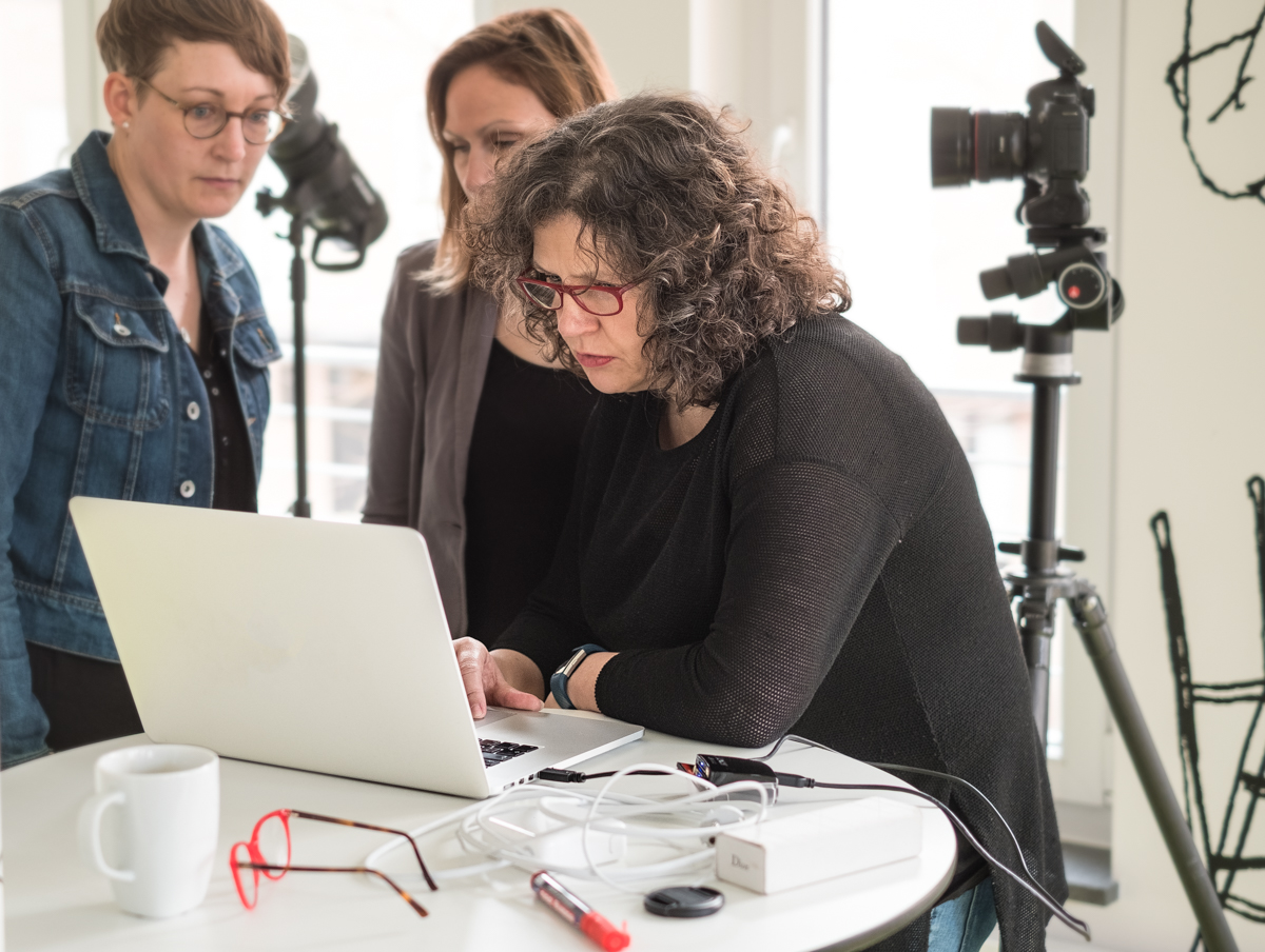 Unternehmerin Simone Naumann arbeitet gemeinsam mit zwei Frauen an einem Laptop, um Bildsprache, Inhalte und visuelle Strategie praktisch weiterzuentwickeln. Die Szene zeigt konzentrierte Zusammenarbeit, unternehmerisches Denken und die professionelle Umsetzung visueller Kommunikation.