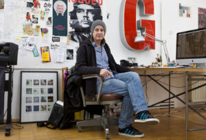 Mann in kreativem Büro vor Posterwand und Schreibtisch.